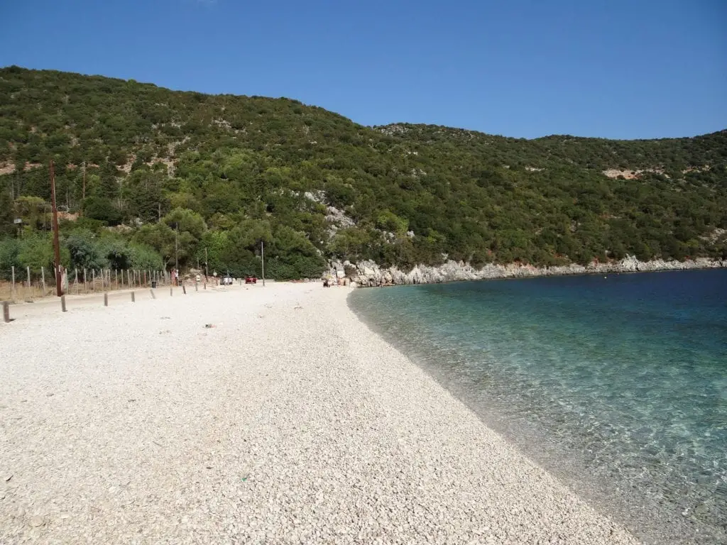 Pristine pebble beach against a backdrop of dense green hills and crystal-clear waters