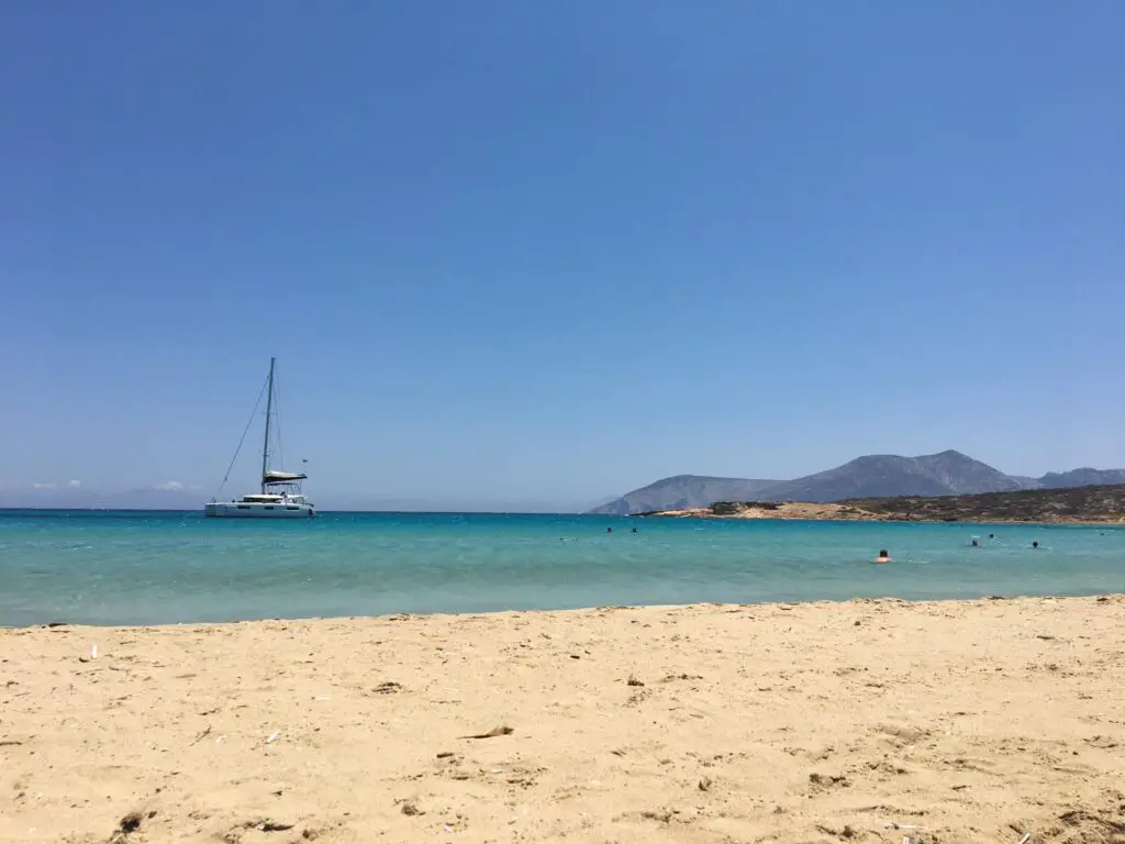 A serene beach scene in Koufinisi with a yacht sailing past. 