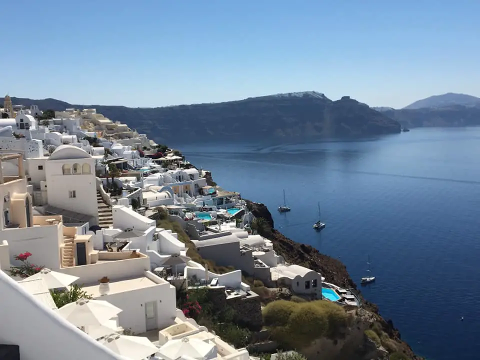 A stunning view of Santorini’s cliffside, with white buildings and blue-domed roofs cascading down to the sparkling Aegean Sea.