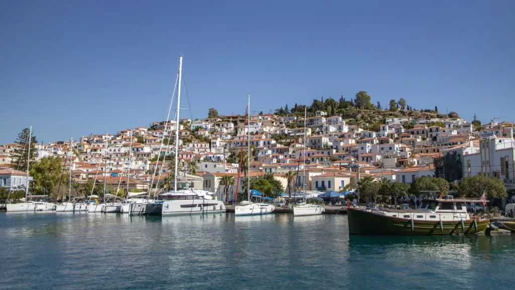  a panoramic view of a bustling port town with colourful buildings densely packed along the waterfront, reflecting in the tranquil waters of the harbour. 