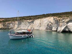 A serene cove on Milos with a sailing boat moored in crystal-clear turquoise waters, surrounded by stark white cliffs, perfect for leisurely exploration.