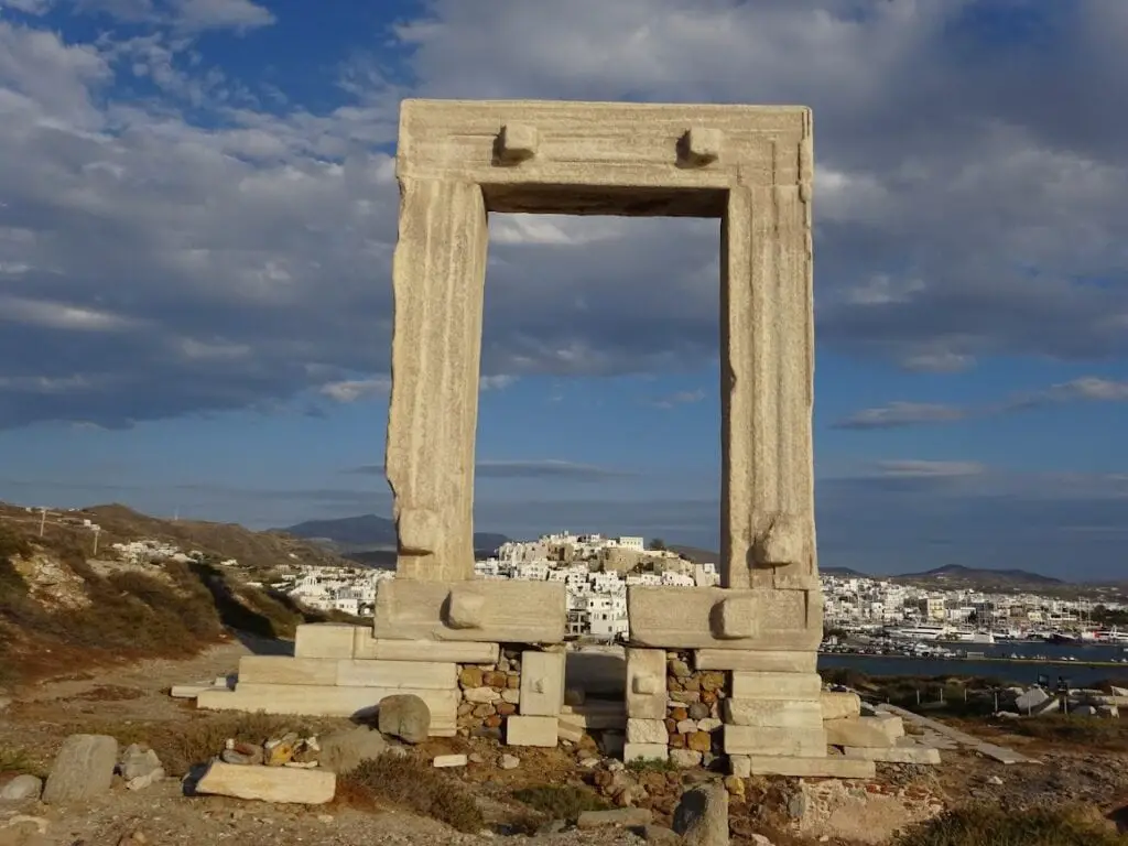 A scenic view of Naxos Town with its classic Cycladic architecture; white and pastel-colored houses densely packed along the hillside overlooking a tranquil sea, reflecting the quintessential charm of the Greek islands.