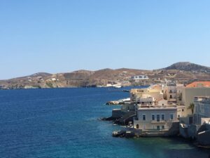 Coastal view in Ermoupoli, Syros, featuring neoclassical buildings along a calm bay under a clear blue sky, highlighting the architectural elegance of the Cyclades.
