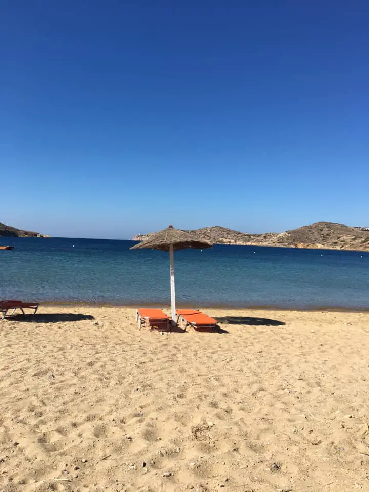 A tranquil beach scene in Ios, featuring clear waters, golden sand, and a typical beach umbrella, epitomizing the idyllic Greek island getaway.
