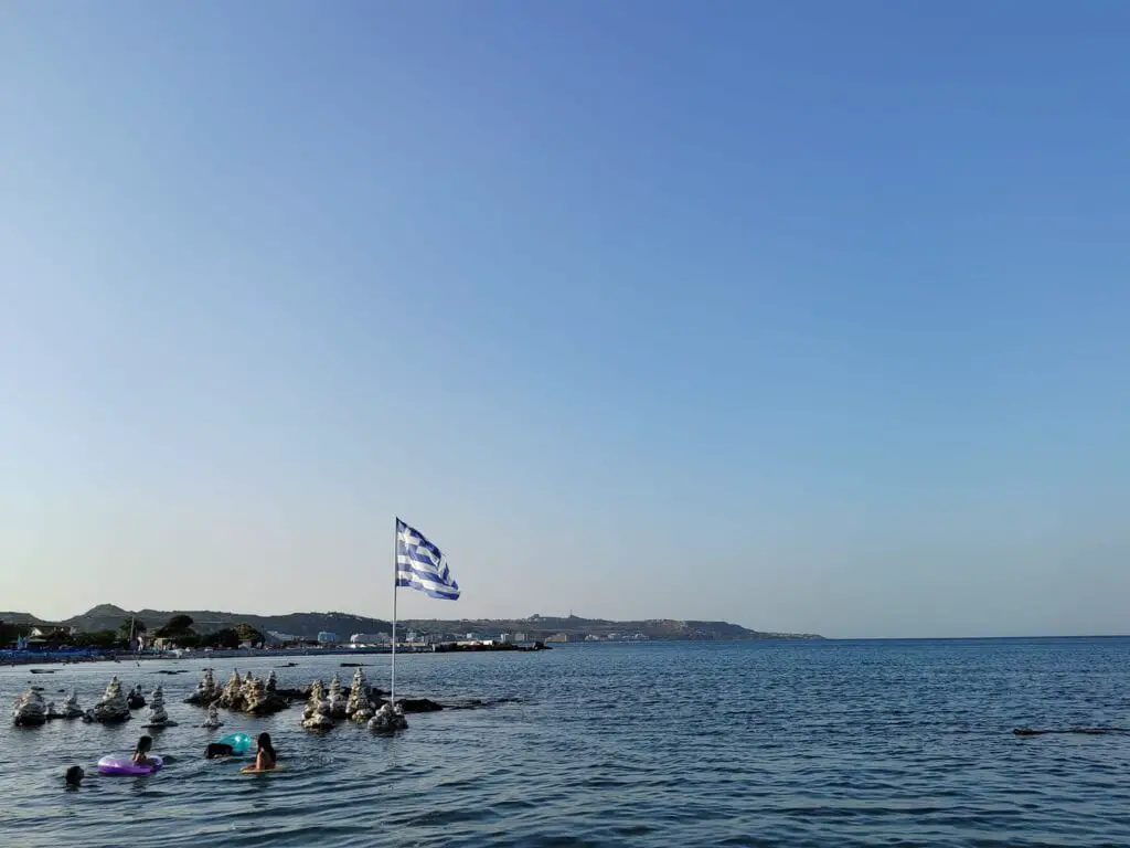 people swimming in Rhodes Greece with the greek flag as a backdrop