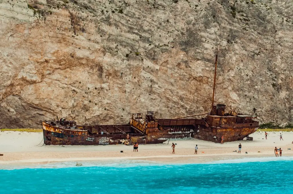 A sunken ship rests on Navagio Beach, surrounded by cliff and sea.